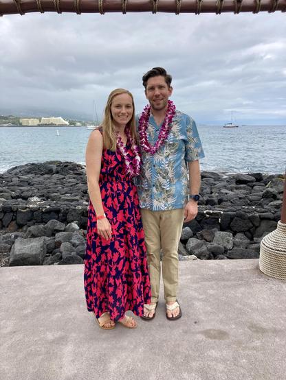 A photo of Megan and me in luau wear in front of the ocean.