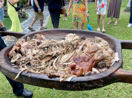 A photo of two men removing a whole pig from its underground oven.