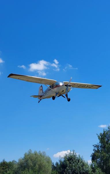Aircraft from below in final approach. Blue sky with some high little clouds. Trees can be seen at the bottom.