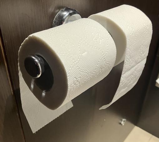 A toilet roll holder that holds two rolls. One has the loose end towards the wall, the other has it away from the wall.