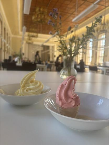 Das Bild zeigt zwei Schälchen mit einem Erdbeeren- und einem Vanille-Softeis - im Hintergrund ein Blumenstrauß.