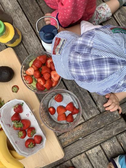 Das Bild zeigt Kinder von oben, die vor Trinkflaschen und roten Erdbeeren sitzen.