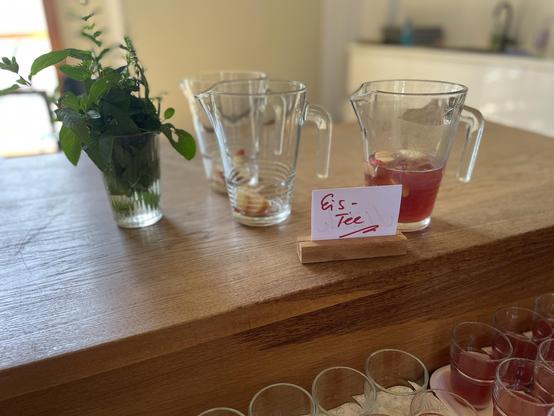 Das Bild zeigt drei Kannen, frische Minze und Gläser mit dem Schild "Eis-Tee".