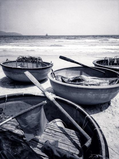 An above view of several basket boats, used by Vietnamese fisherman, most filled with paddles and various netting, lie high up on the dry sand, awaiting their next sea voyage