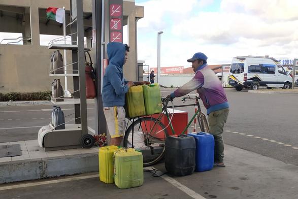Deux personnes en train de charger un vélo avec 6 bidons de 20L remplis d'essence.
