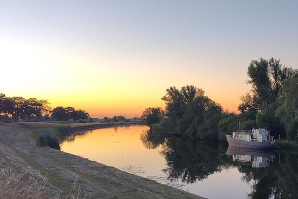 Sunset over a river with its glow reflecting in the water. A small moored boat visible.