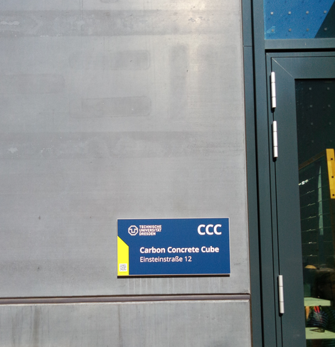 Ein blaues Schild an grauer Betonwand trägt die Aufschrift CCC Carbon Concrete Cube.
