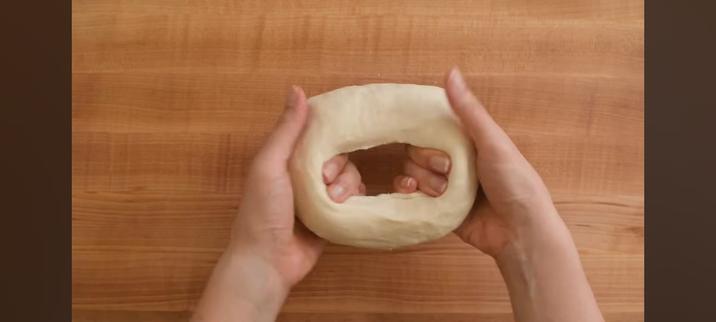 Someone making dumpling wrapper dough. They just made a hole in a ball of dough and are making the hole bigger using both of their hands.