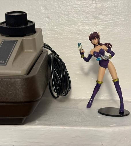 A small toy of Nei from Phantasy Star II looks to her left, a giant (compared to her) Sears-branded Atari pong console