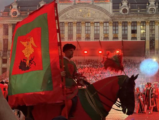 Grand Place in Brussels with a horse in the center and a person holding the flag of the city.