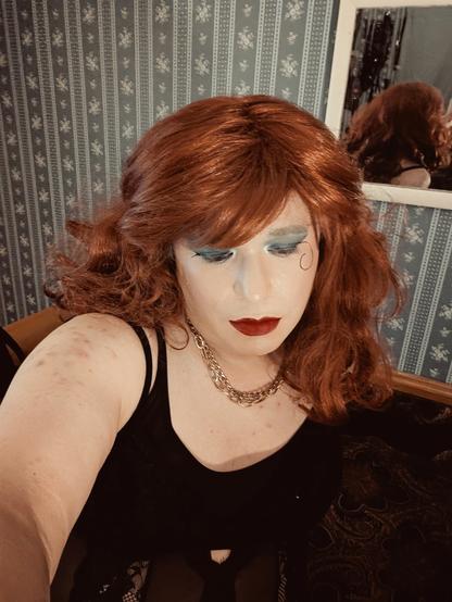 I am taking a selfie. I am wearing a black top, a red wig, and makeup.