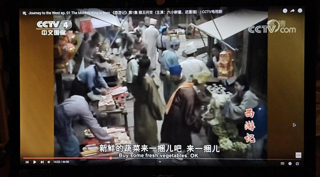 Studio setup of a market street in a non-descript Chinese town in an undefined historical era. People in hanfu are walking between the stalls where sallat, writing stuff, and other things are sold.