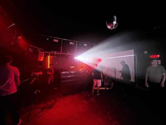 The Carpet Shop club during setup. hazy red light, a bright white projector beam pointing just off camera, a big dj booth