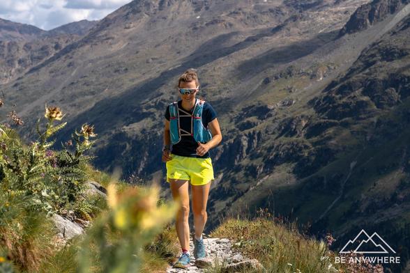 Trailrunnerin auf einem schmalen Bergpfad im Val Roseg, umgeben von alpiner Vegetation mit felsigem Gebirge im Hintergrund.