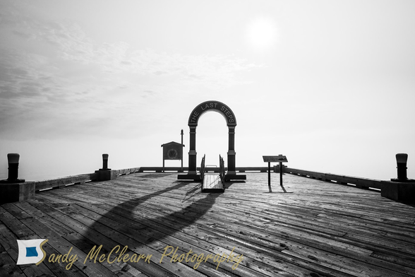 Arch casting a shadow on a wharf in silhouette against a foggy background.