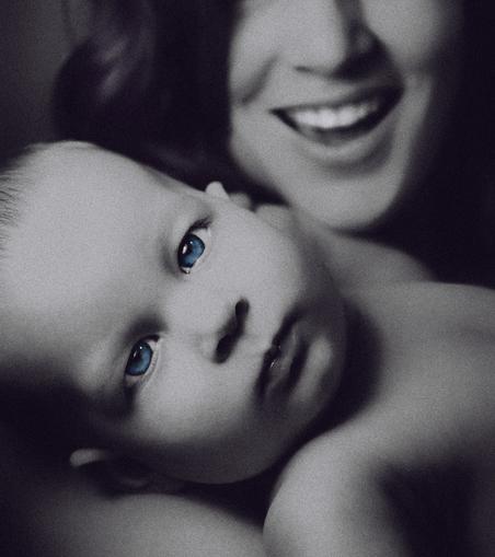 portrait of baby Eden looking serenely into the camera while her mother coos her on in the distance