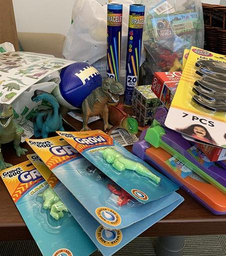 A table full of workshop materials (a.k.a. toys) that I packaged and sent to the IRDL Scholars. There are small plastic dinosaurs, glow bracelets, stick-on moustaches, foam footballs, etc.