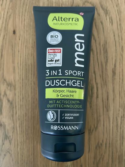Das Bild zeigt eine Tube Duschgel der Marke Alterra Naturkosmetik, speziell für Männer. Hier ist eine detaillierte Beschreibung des Produkts, wie es auf der Verpackung zu sehen ist:
⸻
Produktbeschreibung (Vorderseite der Verpackung):
• Marke: Alterra Naturkosmetik
• Produkttyp: 3 in 1 Sport Duschgel
• Anwendung: Für Körper, Haare & Gesicht
• Zertifizierung:
• Mit Bio-Inhaltsstoffen
• Zertifiziert vegan
• Dufttechnologie: Mit Actiscent®
Dufttechnologie
• Testurteil:
• ÖKO-TEST: Sehr gut (Magazin 04/2022)
• Händler: ROSSMANN
⸻
Die Verpackung ist überwiegend dunkel gehalten mit hellgrünen und weißen Akzenten. Die Tube hat einen Klappverschluss am unteren Ende und steht aufrecht.