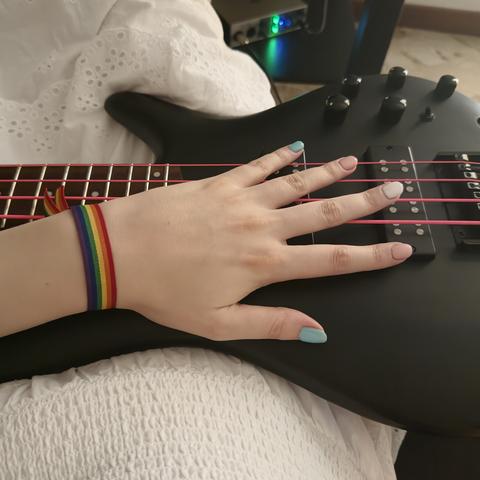 My left hand resting on my bass. My nails are like the trans flag and I’m wearing a rainbow bracelet