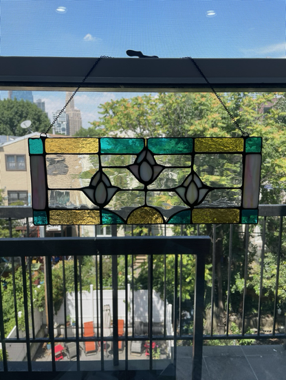 a stained glass piece in a window with three little white flowers and a border of yellow and blue