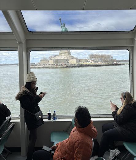The Statue of Liberty, sliced in two by the cruise ship windows. One rider looks out, the others look at their devices.