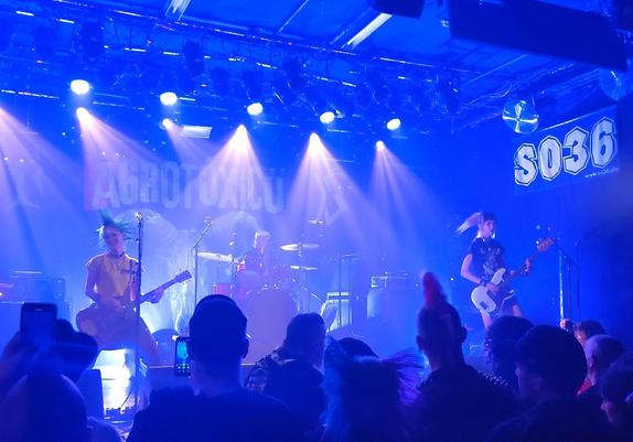 Rumkicks on stage - left side is the singer who plays guitar - she has green spikes and green mohawk and wears a yellow shirt. the bass player is on the right side, she hase a black white ponytails. and the also female drummer is in the back, but you can't see her really on this picture