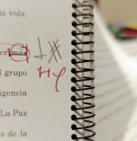 En el margen de una hoja impresa y engargolada con espiral metálica, se ven marcas de corrección en negro y rojo.