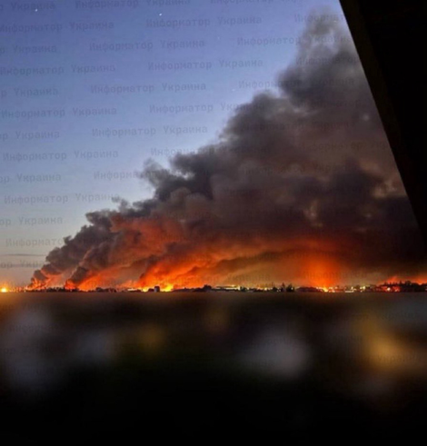A wide shot of the sky over Kyiv, with a wide curtain of thick smoke, glowing red from the fires below.