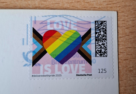 Briefmarke mit dem Text: "Love is Love" und einem Herz, mit den Regenbogenfarben ausgefüllt. Und klein der Hashtag #deliveredwithpride2025.