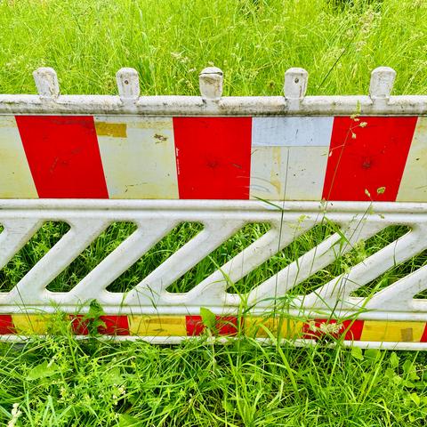 A weathered plastic fence with red and yellow stripes, partially obscured by tall green grass and weeds.