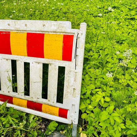 A weathered plastic fence with red and yellow stripes stands in a lush green field with small white flowers.