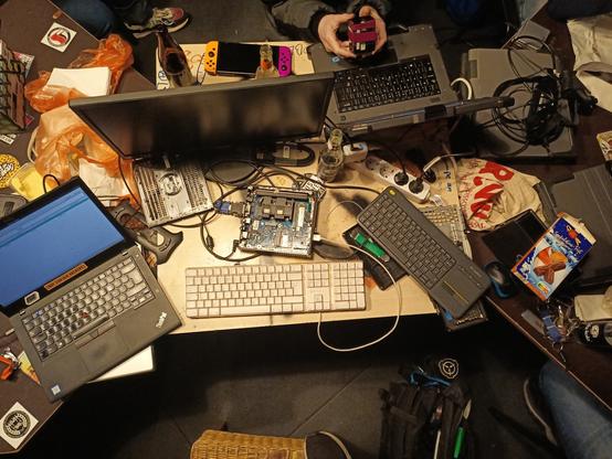 Ein Tisch in der Draufsicht es liegen zwei Tastatur und ein Mini pc vor einem Monitor links ein Laptop dem Fotografen zugewandt rechts einer der von der Gegenüber Liegen Seite bedient wird