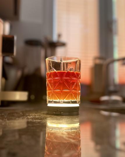 Ein Foto eines Whiskeyglases, gefüllt mit Kaffee. Das Glas ist von unten beleuchtet, der Kaffee schimmert transparent rötlich. Der Hintergrund ist verschwommen, das Getränkt wirkt edel