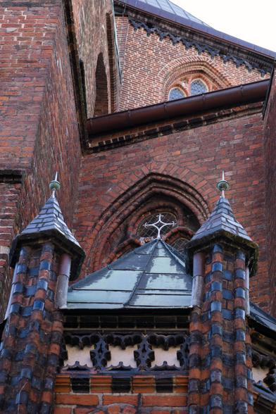 Photo from a brick chruch. Two decorative tower elements with a roof in between with a cross on top. Behind the cross is a part of a church window.

The perspective creates a lot of diagonal lines between making it a bit confusing.
