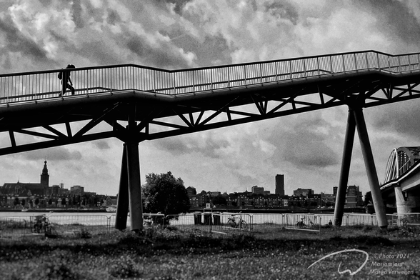 A silhouette of a person walking up a bridge against the view of the city in the background with a stormy sky above.