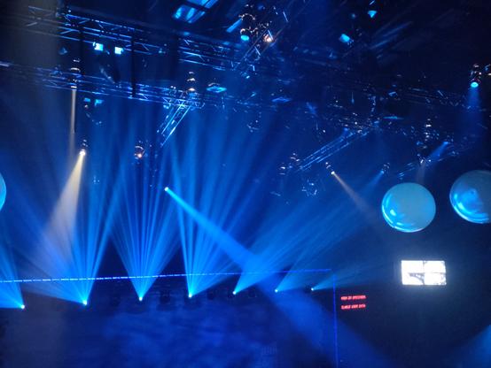 Der Blick an die Decke eines Musicaltheaters. Man erkennt schemenhaft Traversen, viele Scheinwerfer und andere Technik. Alles ist in ein blaues Schummerlicht getaucht. Man sieht etliche Scheinwerferstrahlen im leichten Nebel.