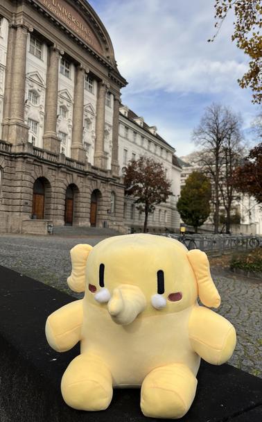Das gelbe Mastodon-Maskotten, an der Uni Innsbruck heißt es Federike, sitzt vor dem Hauptgebäude der Uni, ein historischer Altbau.