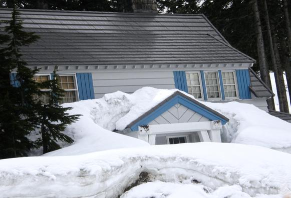A white house with blue decorative shutters is covered in snow all the way to the top few inches of a mid-level maybe bay window. To the left, some trees presumably in the front yard are also showing just their tops. There are also some taller windows on the top floor that are almost completely unobstructed. However, the snow, although thick, looks kinda fluffy and I don't know how far you'd sink in if you actually tried to step outside on it. Judging from the lack of footprints, no one has actually tried. 2010. British Columbia. Photo by Peachfront.