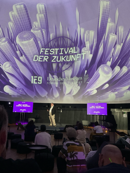 Der Autor Wolf Lotter steht vor einer großen Leinwand mit lila Formen