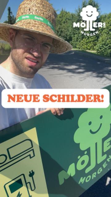 Das Bild zeigt eine Person, die draußen auf einer Straße steht und ein Schild mit dem Logo "Möllers Morgen" hält. Die Person trägt einen Strohhut mit einem grünen Band, auf dem "BayWa" steht, sowie eine Sonnenbrille und ein weißes T-Shirt. Im Hintergrund sind Bäume und ein klarer Himmel zu sehen, was auf einen sonnigen Tag hindeutet.

Über dem Bild ist ein Text mit der Aufschrift "Neue Schilder!" zu sehen, was darauf hinweist, dass es sich um neue Schilder handelt, die möglicherweise für Werbung oder Information verwendet werden. Das Logo "Möllers Morgen" ist sowohl auf dem Schild als auch in der oberen rechten Ecke des Bildes sichtbar.