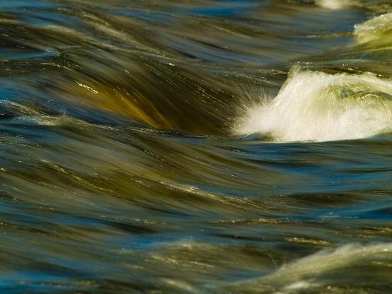 Water Play

This is an abstract closeup of a little spot of the Merced River in Yosemite National Park.
The water is flowing in a sweeping manner over rocks in the river bending the water in beautiful shapes. The water is a deep green with streaks of blue mixed in.
The water near the top of the image sweeps over a rock and the crashes into another submerged rock creating a little bit of white water and a little sparkle in the water.