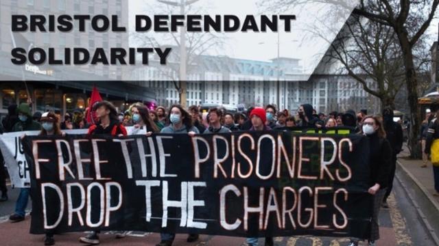 "Bristol Defendant Solidarity" People holding a banner reading "Free The Prisoners | Drop The Charges"