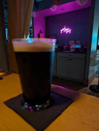 A blurry glass of Guinness in the foreground and an in-focus neon sign in the background reading "good vibes only".