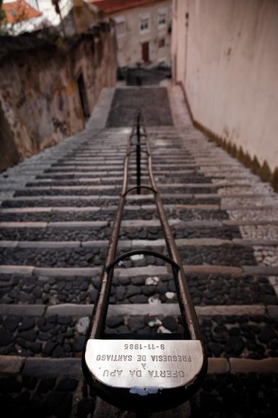 You can see some stairs in Lisbon. A handrail is in the middle. There's an inscription in it: "Oferta da Apu a freguesia de Santiago. 9-11-1985"
