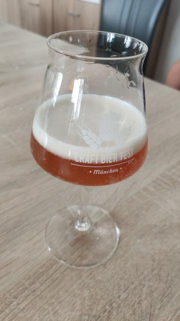 A beer sampling glass with a small amount of golden brown beer with a medium sized foam head