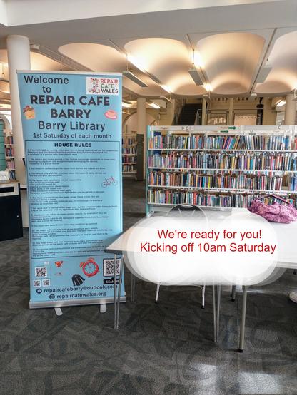 A tall blue sign for Repair Cafe Barry standing beside some tables with shelves and shelves of books behind it. Text overlaid reads "we're ready for you! kicking off 10am Saturday."