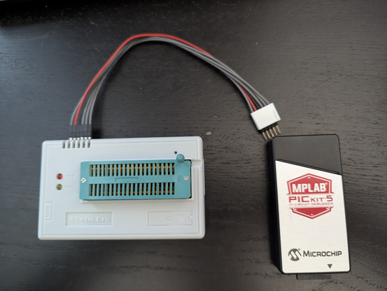 A TL866II device on the left, with a ZIF socket and two LEDs. There's a programming interface cable attached to the side on its left. On the right is an MPLAB PICKit5 programmer device.
