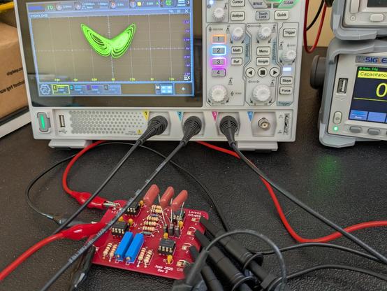 The printed circuit board from the previous post connected to a power supply and oscilloscope. On the scope is the famous Lorenz attractor butterfly.