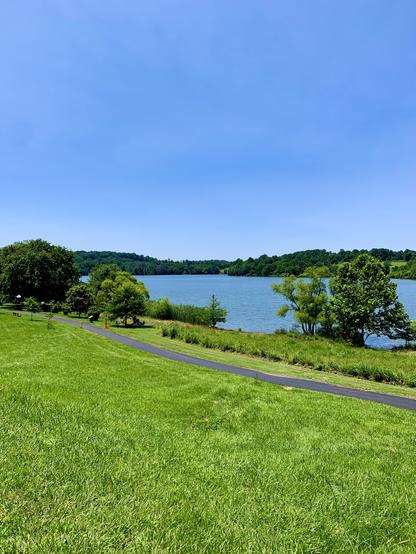A view of Marsh Creek Reservoir on a sunny summer day, seen from a grassy area. A paved trail runs alongside the grass.