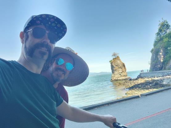 My husband and me posing in front of Siwash rock - the rock formation juts out of the water like a pointy little island. There's a tree on top, but it seems it died a while back. In the foreground you can see me holding the handle bar of one of the bikes we're riding.